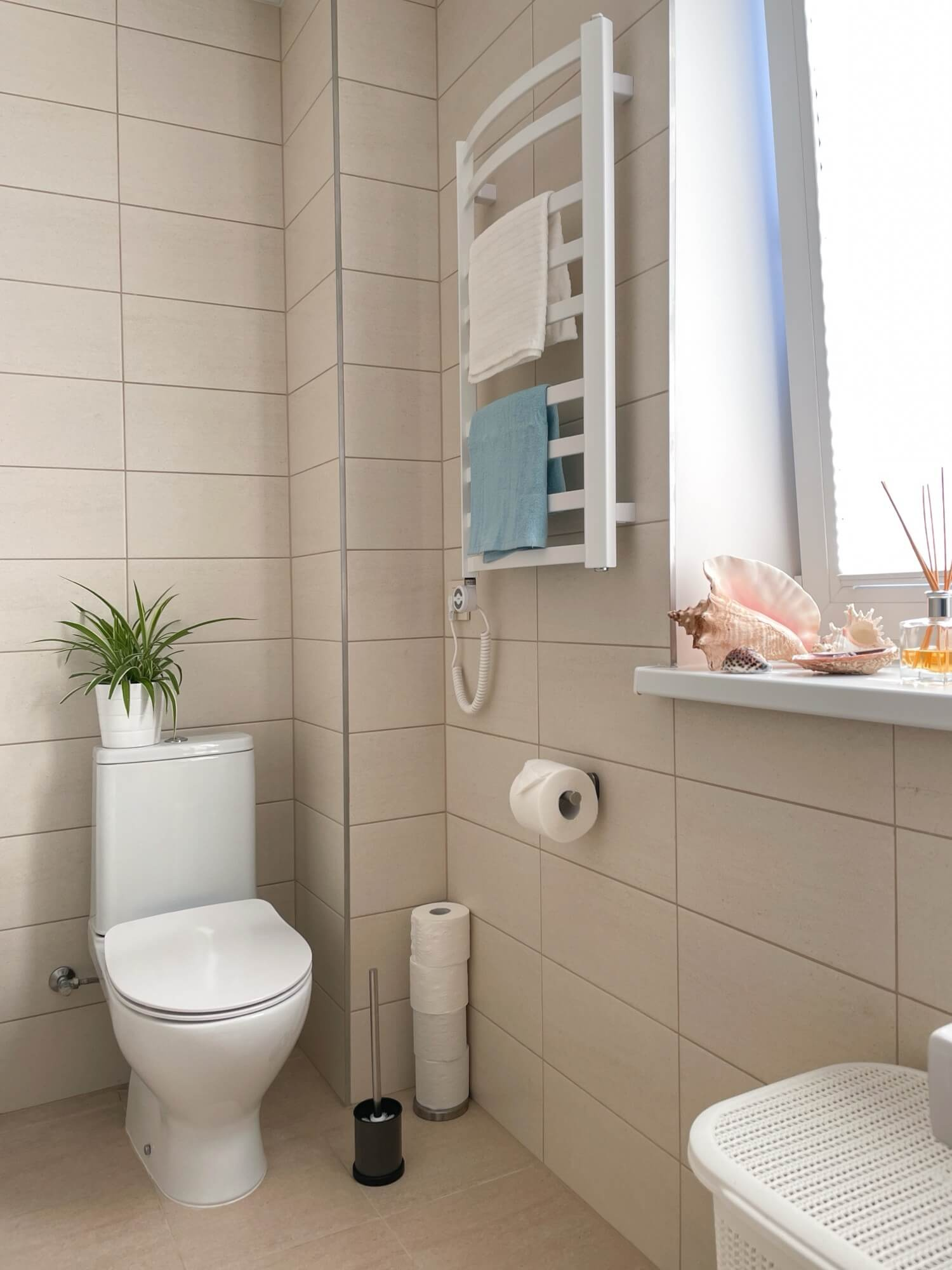 Bright tiled bathroom with toilet and electric heated towel rail by window, typical solution in bathroom renovation.